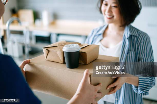 close up of beautiful and cheerful young asian woman receiving home delivery takeaway food order from a delivery man at home. eating at home concept - food and drink industry stock pictures, royalty-free photos & images