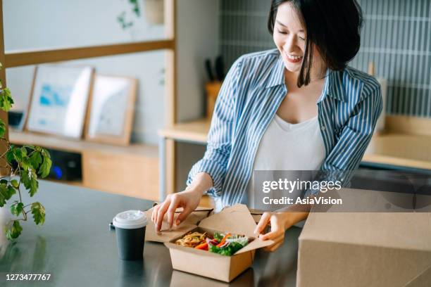 schöne und fröhliche junge asiatische frau öffnen die zumsicht lunchbox mit frischem gesunden salat, essen zu hause mit essen lieferdienste. essen zu hause konzept - take out food stock-fotos und bilder