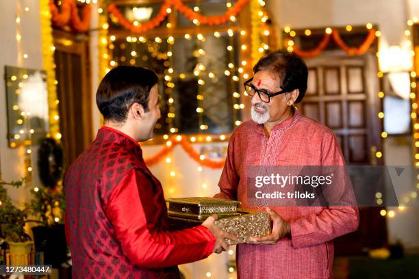beloved son presenting festival greeting gift to elderly father - diwali family stock pictures, royalty-free photos & images