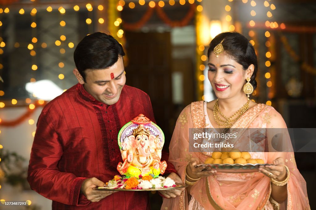 Indian couple carrying statue of Hindu god Ganesh and plate of sweet food