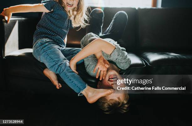 brother and sister playfully wrestling on a black leather sofa - 不穏状態 ストックフォトと画像