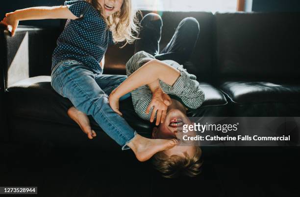 brother and sister playfully wrestling on a black leather sofa - feet girl stock pictures, royalty-free photos & images