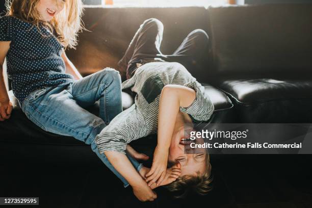 brother and sister playfully wrestling on a black leather sofa - lachen stockfoto's en -beelden