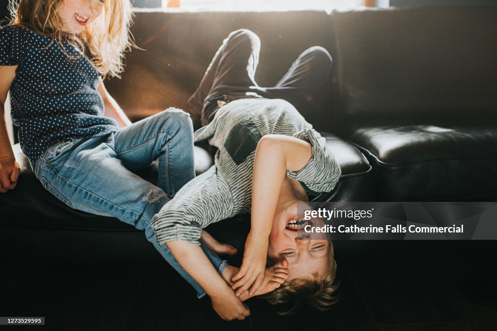 Brother and Sister playfully wrestling on a black leather Sofa