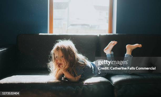 little girl lying on her stomach on a sofa - barefoot feet up lying down girl stockfoto's en -beelden