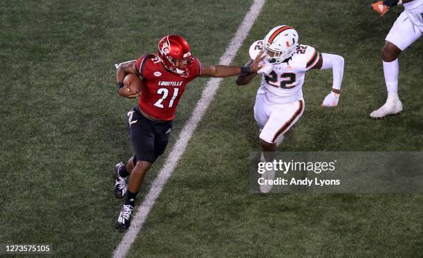 Aidan Robbins of the Louisville Cardinals runs with the ball while defended by Cameron Williams of the Miami Hurricanes at Cardinal Stadium on...