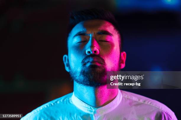 portrait of young man lit by pink and blue neon light in city - modern manhood stock pictures, royalty-free photos & images