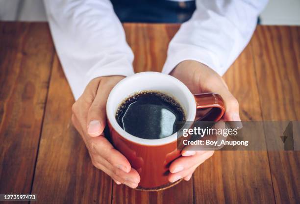 someone hands holding a mug of black coffee before drinking. - caffè americano foto e immagini stock