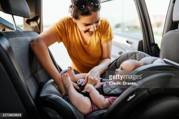 mutter setzt baby-mädchen in kindersitz im auto - baby stock-fotos und bilder