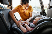 Mother putting baby girl in child seat in the car