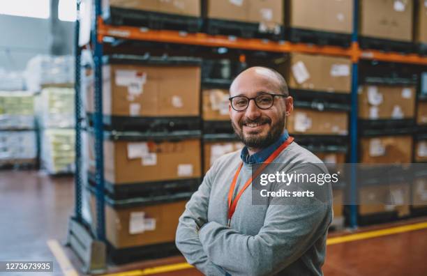 portrait of a smiling businessman standing in corridor of warehouse - business owner stock pictures, royalty-free photos & images