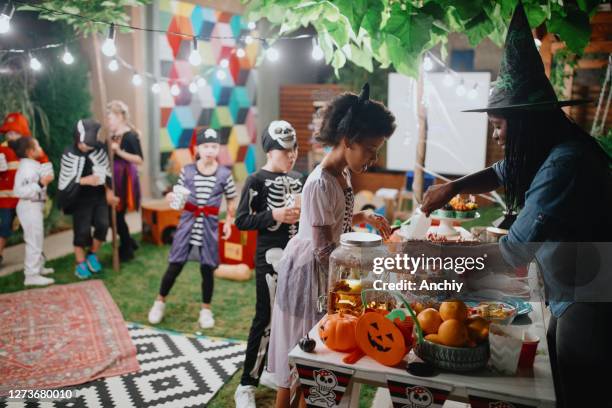 ouder die suikergoed en popcorn aan haar jonge geitjes en hun vrienden bij de filmnacht van de binnenplaats dient - adult halloween party stockfoto's en -beelden