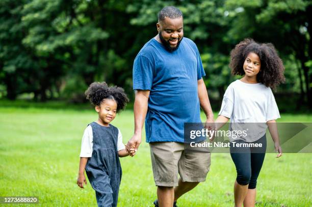 african father and daughters walking in the public park together. simple living, leisure activity. - african american couple walking park ストックフォトと画像