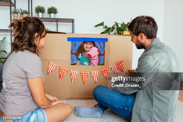 young family at home, watching daughter on the stage behind cardboard box - puppet theatre stock pictures, royalty-free photos & images