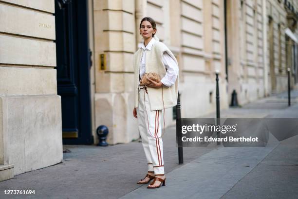 Natalia Verza wears a white sleeveless wool cardigan / vest from Isabel Marant, a white shirt, Balmain white pants with printed brown stripes, a...