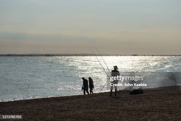 Man fishes as a couple walk along the beach while the sun goes down during recent warm weather on September 20, 2020 in Southend on Sea, London.