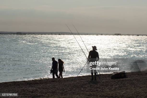 Man fishes as a couple walk along the beach while the sun goes down during recent warm weather on September 20, 2020 in Southend on Sea, London.