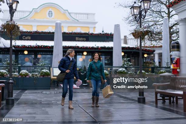 vrouwen die van kerstmiswinkeling in openluchtwinkelcentrum genieten - outlet stockfoto's en -beelden