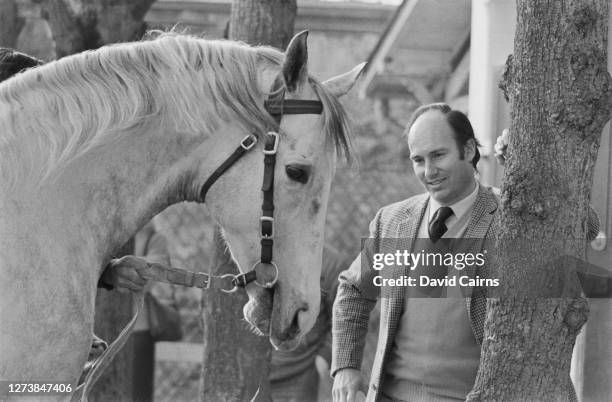 Aga Khan IV, wearing a tweed jacket over a sweater with a shirt and tie, as he stands with his horse Zeddaan, United Kingdom, 18th March 1973.