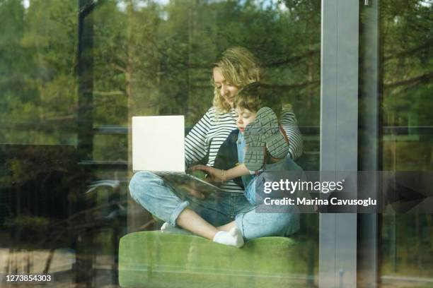 view from the outside on woman working remotely with her laptop and her little child sitting on her knees. - person looking through window stock pictures, royalty-free photos & images