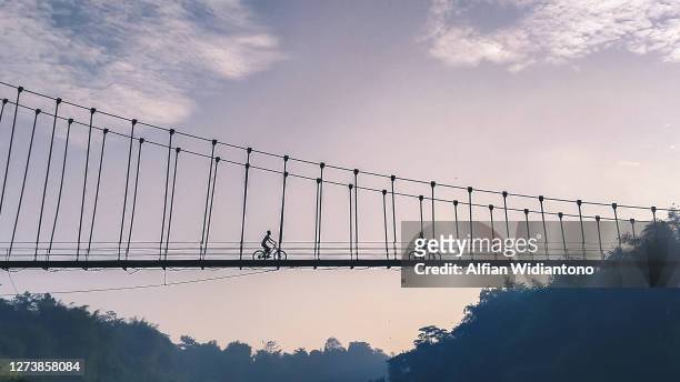 riding bike crossing river through suspension bridge - asia village river bildbanksfoton och bilder