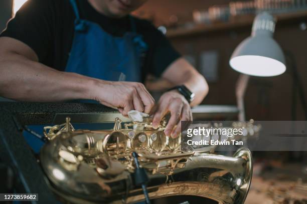 asian chinese male expertise repairing restoring alto saxophone at his work place - woodwind instrument stock pictures, royalty-free photos & images