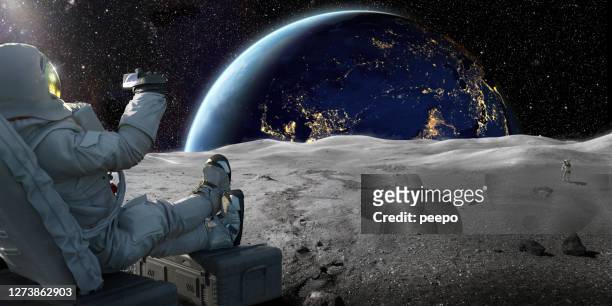 astronaut sitzt auf mond aufnahme sonnenaufgang auf der erde mit smartphone - textfreiraum stock-fotos und bilder
