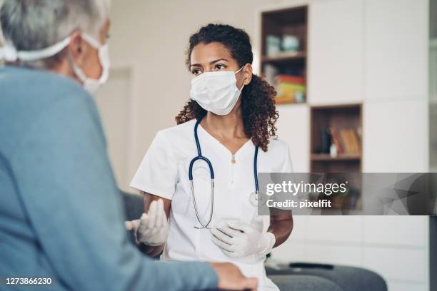 young female doctor talking to a senior patient - female doctor with mask stock pictures, royalty-free photos & images