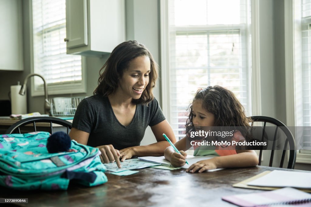 Father helping young girls with schoolwork at kitchen table