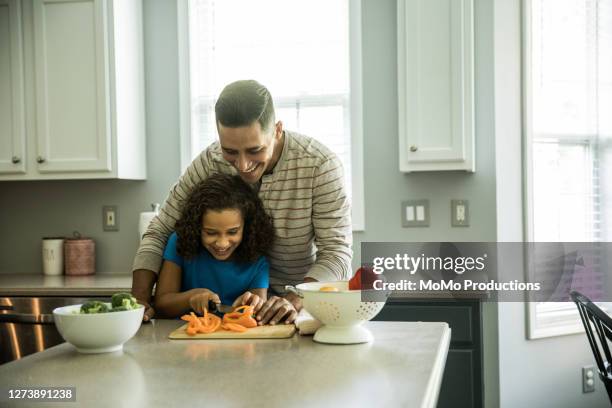 father teaching daughter to cut vegetables in kitchen - leanincollection father stock pictures, royalty-free photos & images