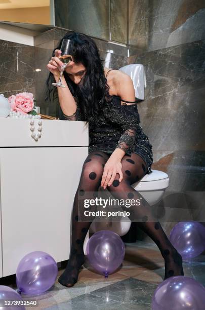 betrunkene junge frau sitzt auf der toilette mit glas wein in den händen - erbrechen stock-fotos und bilder