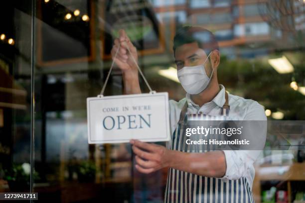 man working at a grocery store wearing a facemask and hanging an open sign on the door - supermarket mask stock pictures, royalty-free photos & images