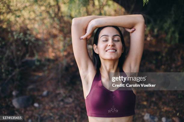 young latina woman stretching in nature after a workout with her arms raised - beha stockfoto's en -beelden