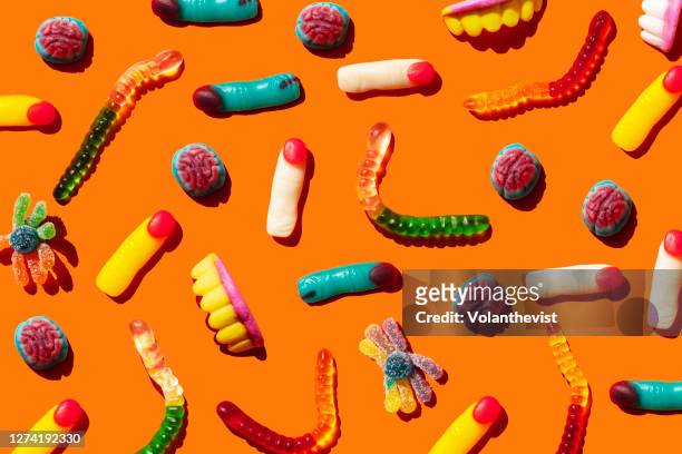 halloween jelly beans, finger-shaped, brains, worm and vampire teeth on orange background - halloween stock pictures, royalty-free photos & images