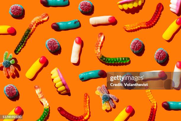 halloween jelly beans, finger-shaped, brains, worm and vampire teeth on orange background - coinfeitos imagens e fotografias de stock