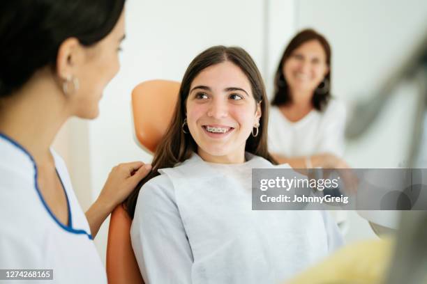 gelukkige tienerpatiënt die bij vrouwelijke tandarts glimlacht - orthodontics stockfoto's en -beelden