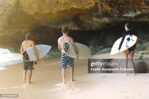 three people with surfboards on beach, uluwatu, bali, indonesia - uluwatu stock pictures, royalty-free photos & images