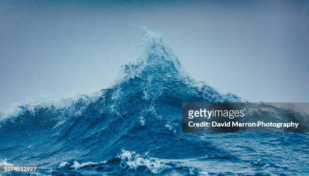two large swells meet and create a large peak of powerful ocean - onda foto e immagini stock