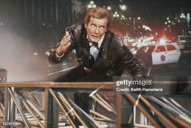 Matte shot of English actor Roger Moore as 007, clinging to a fire engine ladder in a publicity still for the James Bond film 'A View To A Kill',...