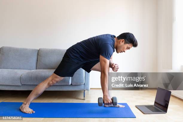 man watching online video and doing dumbbell exercises at home - home workout stockfoto's en -beelden