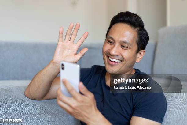 man having a video call on his cell phone at home - navy blue living room stock pictures, royalty-free photos & images