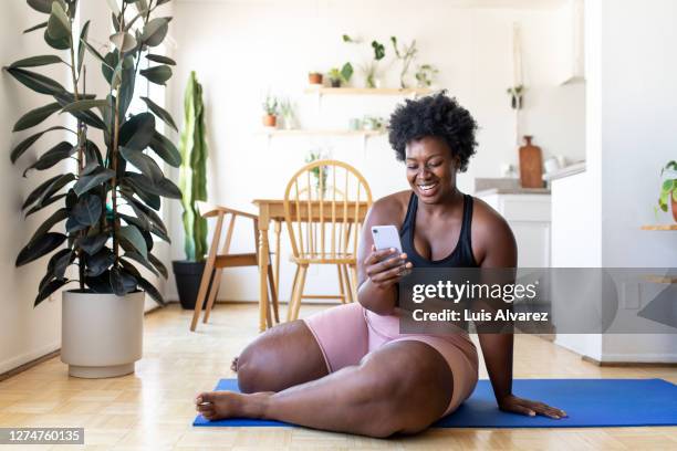 woman using phone after exercising at home - black woman yoga stock pictures, royalty-free photos & images