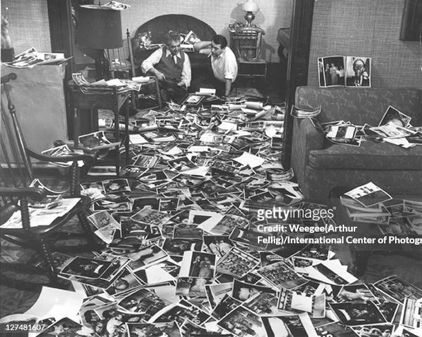 American photographer Weegee and collaborator Mel Harris sit on the floor and look through dozens of the former's photos, strewn across the floor,...