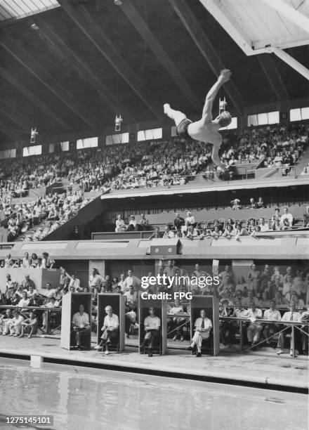 Four judges sit within their enclosed booths at the edge of the pool with spectators behind as American driver Bruce Harlan makes his final dive of...