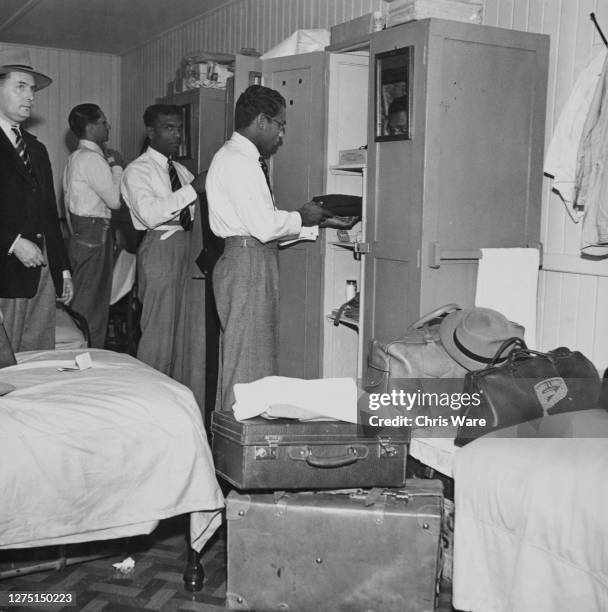 Male athletes from Ceylon settle into their accommodation, packing their clothes away into wardrobes at their quarters in an army camp in Richmond...