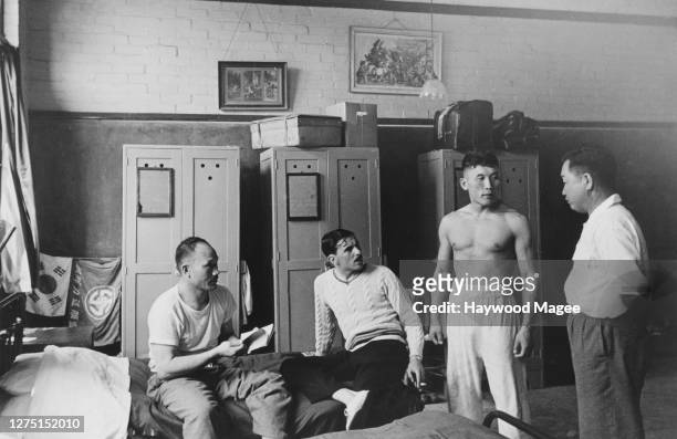 Male athletes of the Korean team talking with their hostel manager, in the background are three wardrobes and two flags , in their accommodation at...