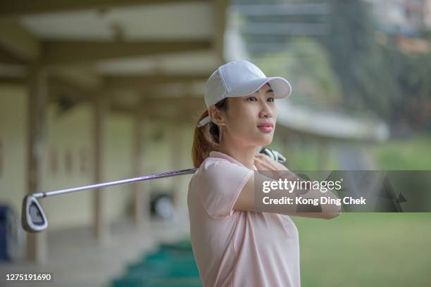 young asia chinese woman golfer teeing off and swing her driver at golf driving range during rainy day. - driving range stock pictures, royalty-free photos & images