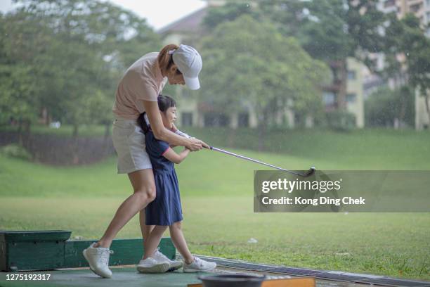 asia chinese mother guide daughter golf lesson at driving range during rainy day. - family golf stock pictures, royalty-free photos & images