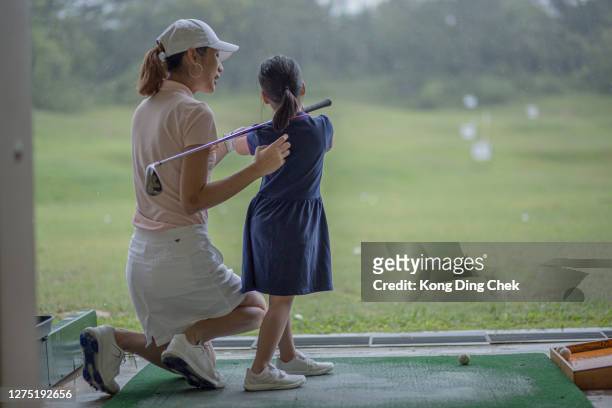 亞洲中國母親在雨天在練習場指導女兒高爾夫課程。 - driving range 個照片及圖片檔