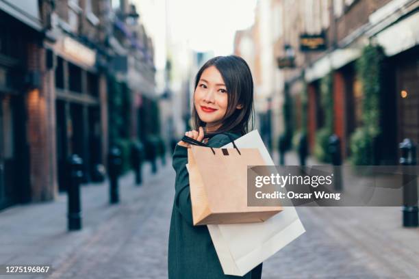 young woman with shopping bags walking on city street - einzelhandel portrait stock-fotos und bilder